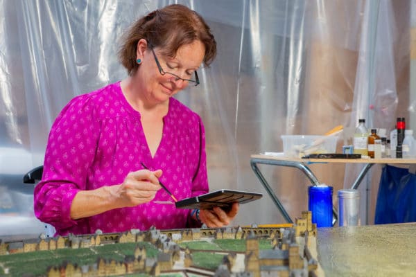 Das Bild zeigt die Chefrestauratorin vor einem Miniatumodell der Stadt Köln. Sie blickt auf einen Farbkasten in ihrer Hand.