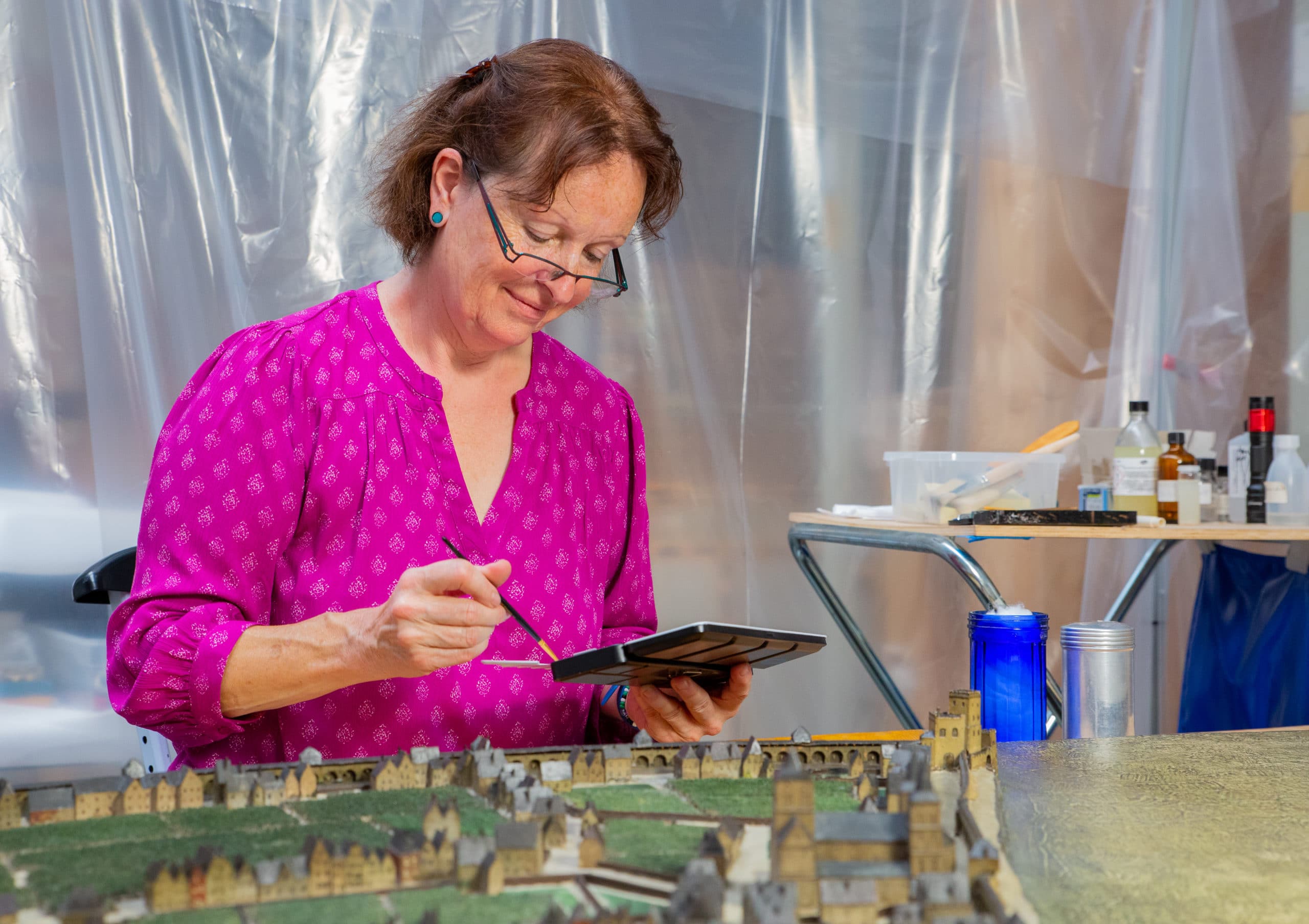 Das Bild zeigt die Chefrestauratorin vor einem Miniatumodell der Stadt Köln. Sie blickt auf einen Farbkasten in ihrer Hand.