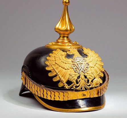 Man sieht eine schwarze Pickelhaube. Die Spitze, der Adler auf der Vorderseite sowie der Rand der Haube sind golden.