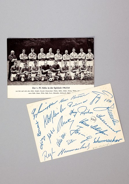 Das Bild zeigt ein Foto der Mannschaft des 1. FC Kölns aus dem Jahr 1963. Auf der Rückseite haben alle Mitglieder unterschrieben.