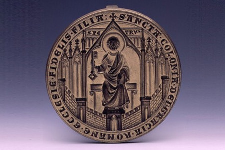 Man sieht eine alte Münze. Auf ihr ist ein Heiliger zu sehen und eine lateinische Inschrift.