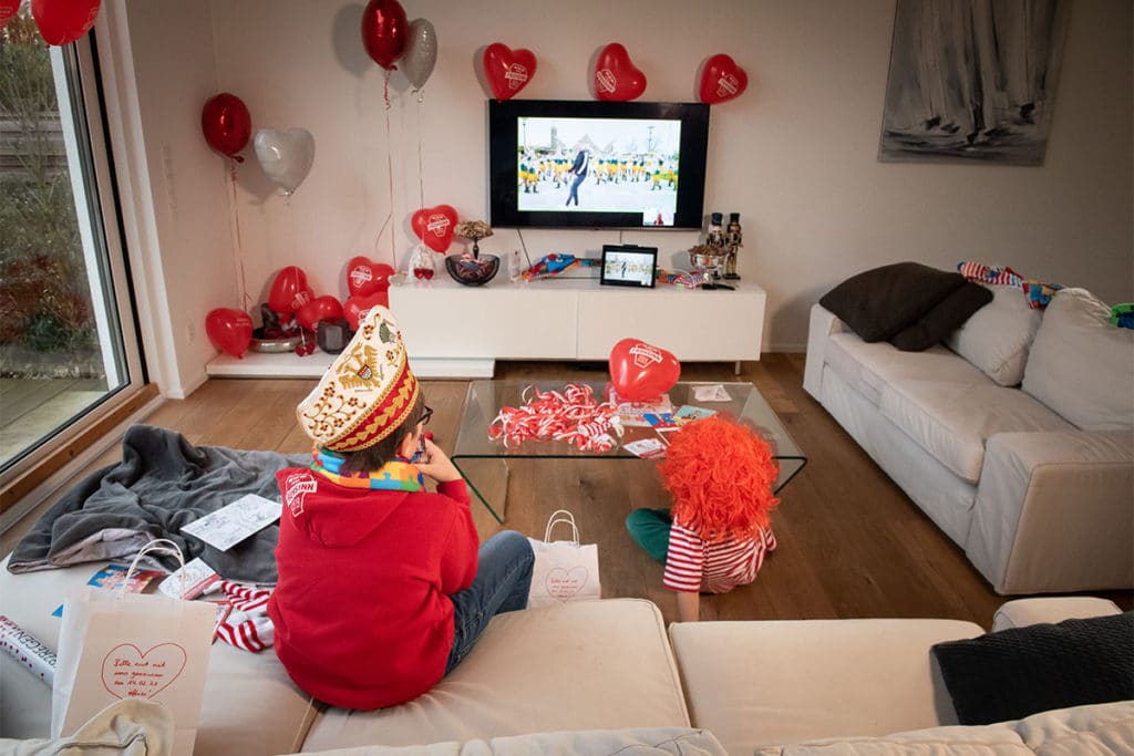 Zu sehen sind zwei Kinder, die die Karnevals-Veranstaltung im Fernsehen mitverfolgen.
