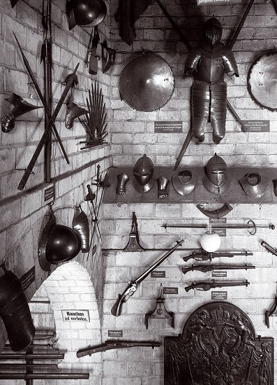 Man sieht mehrere Gegenstände und Waffen einer Ritterrüstung. Diese hängen an einer Burgwand.