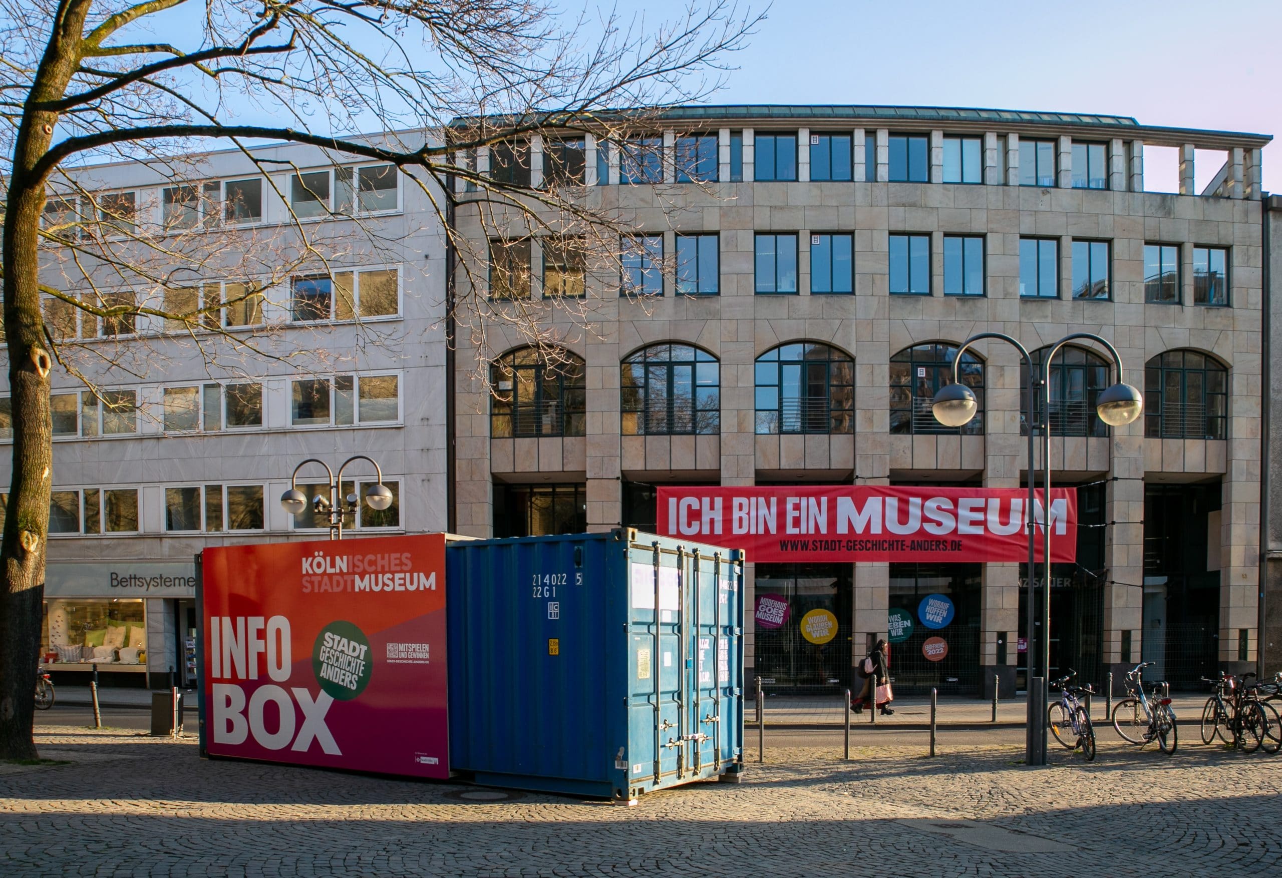 Auf dem Bild sieht man die aufgestellte Museums-Info-Box vor dem neuen Museum. Es ist ein blauer Container.