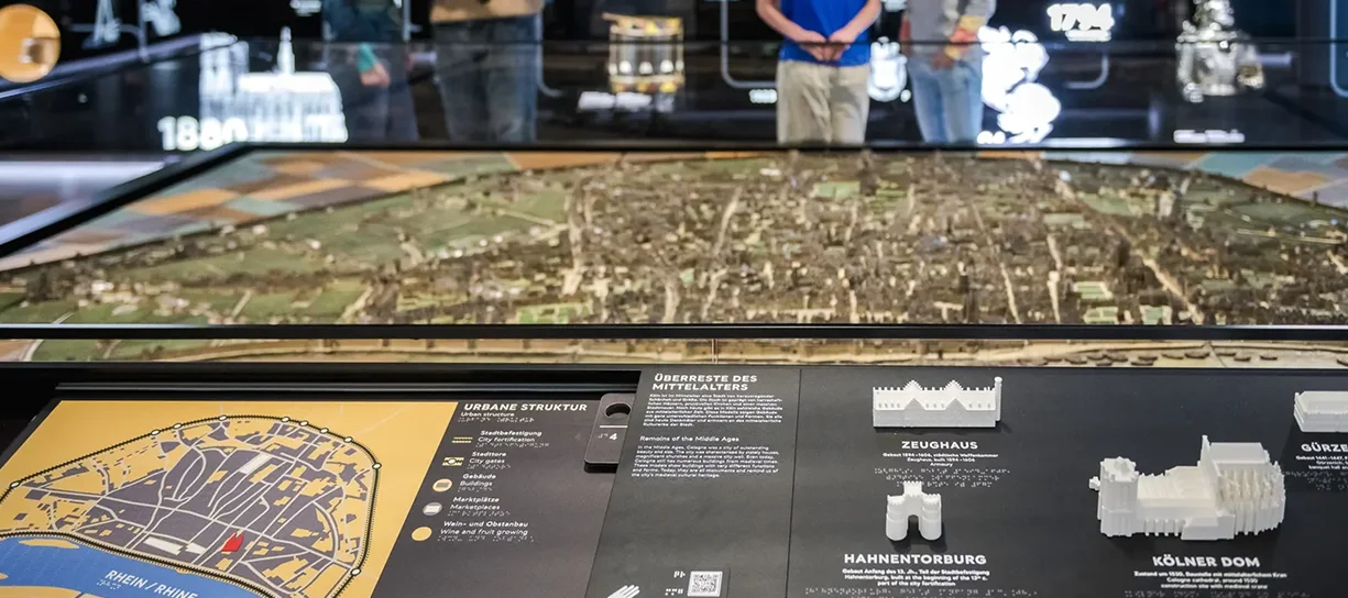 Besucherinnen und Besucher stehen um das beleuchtete große Stadtmodell im Auftaktraum des Museums