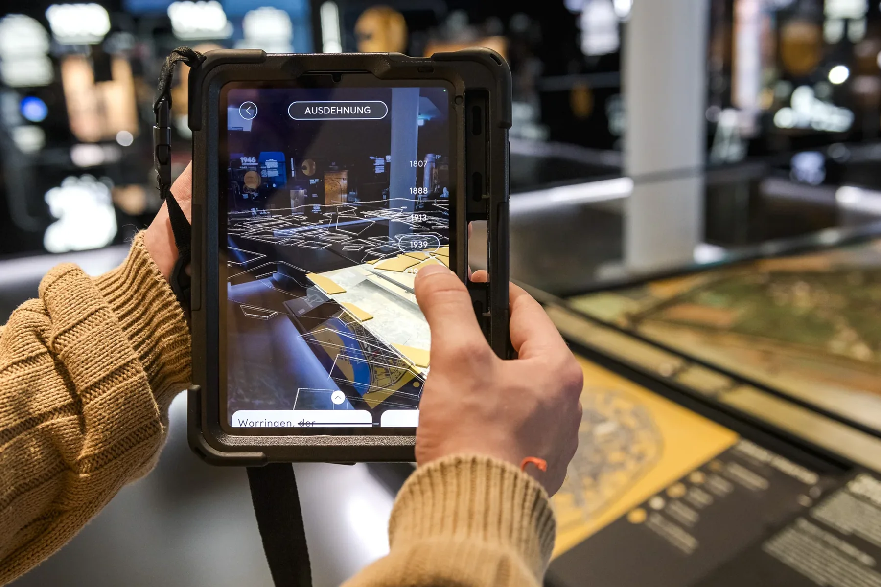 Besucher hält ein Tablet über das Stadtmodell, auf dem Bildschirm erscheinen Zusatzinformationen