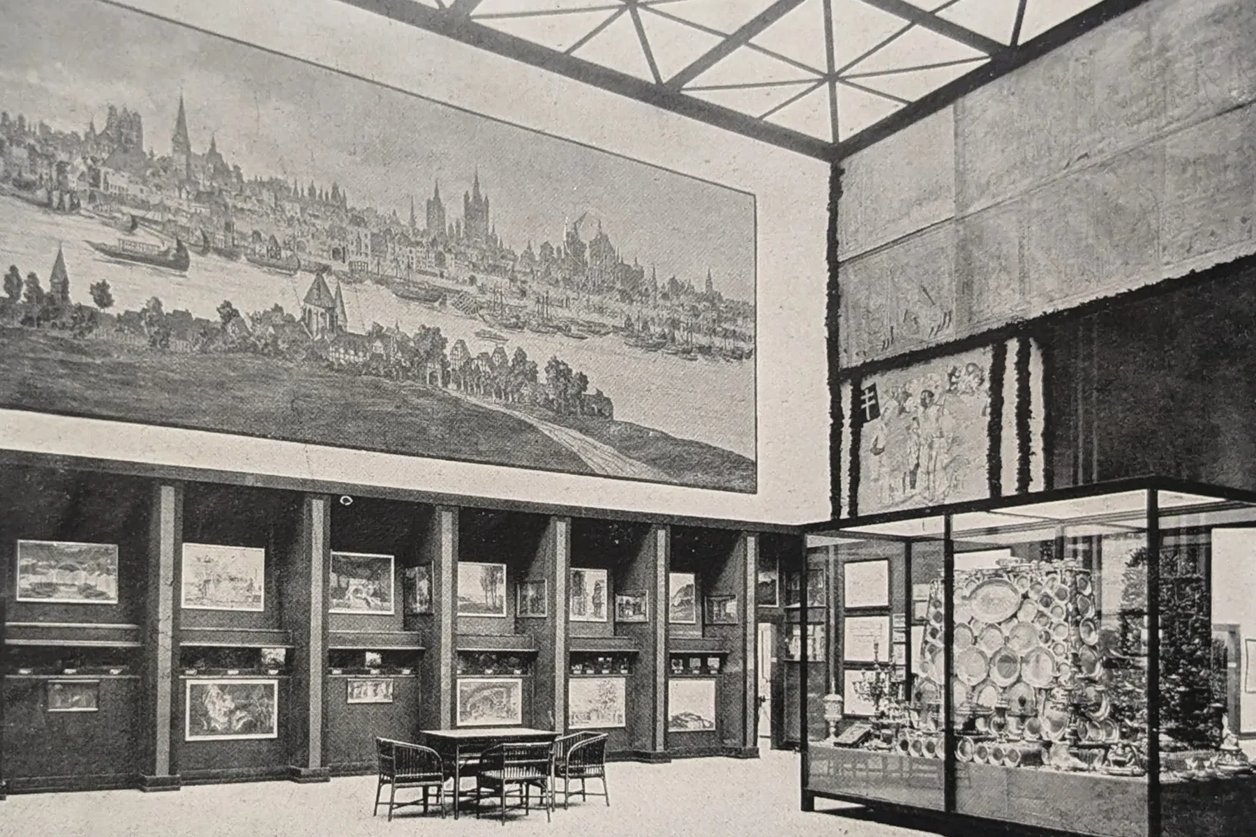 Historische Aufnahme eines Ausstellungsraums mit großem Stadtpanorama an der Wand und einer Vitrine davor