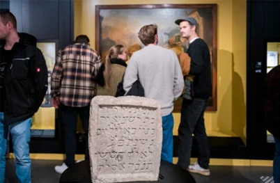 Besucher werden durch die Ausstellung geführt, im Vordergrund ein Stein mit einer Inschrift