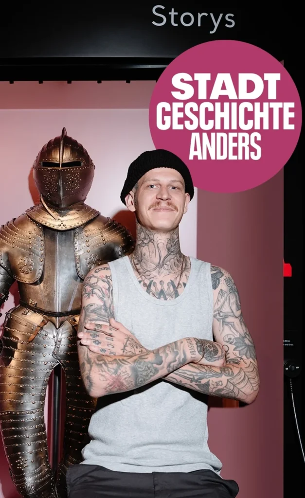 Besucher mit Mütze und tätowierten Armen neben einer Ritterrüstung, dazu der Störer „Stadt Geschichte anders“